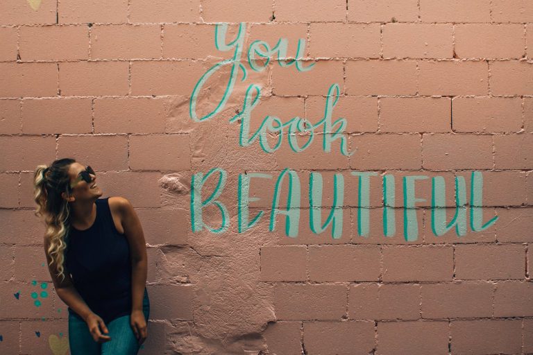 Imagem de uma mulher sorrindo em frente a uma parede escrito: você está linda