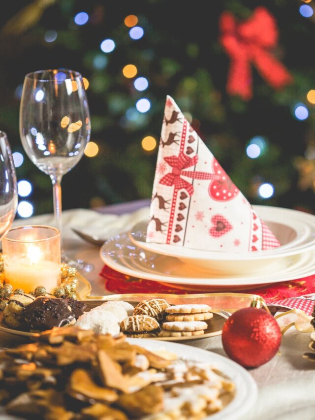 Story 6 Jantar de natal: mesa de natal com prato com guardanapo natalino em cima da mesma, com taças encima da mesa, bolinhas e pinhas de decoração e comida sobre a mesa, e ao fundo uma árvore-de-natal
