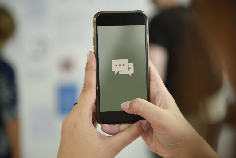 golpe do falso encontro: Mão feminina segurando celular com aplicativo de mensagem na tela