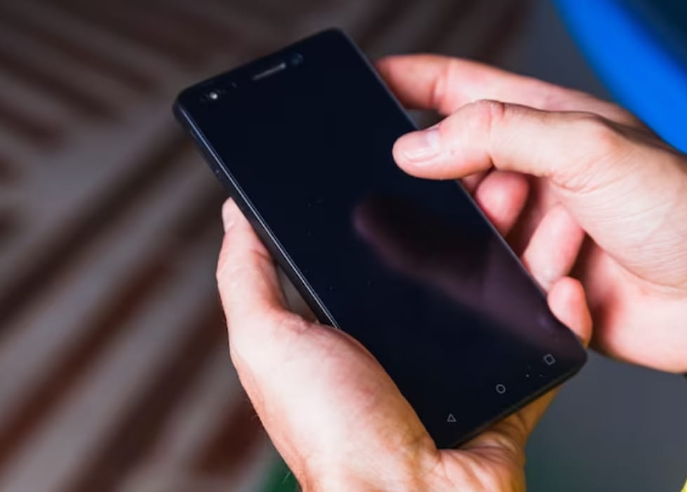 Mão de homem segura celular com tela desligada tentando descobrir como desbloquear o celular sem senha